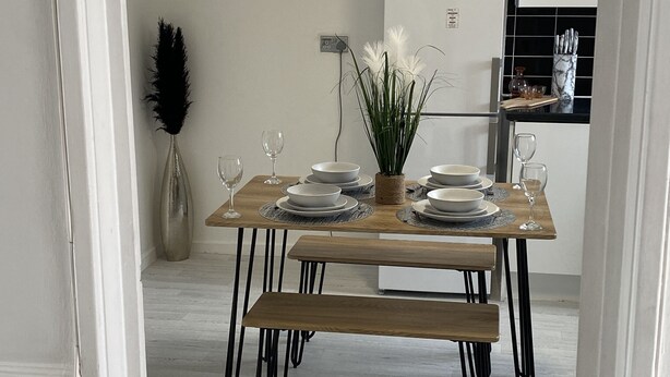 Comedor con mesa de madera dispuesta para cuatro personas, patas de metal negro y una lámpara de techo blanca.