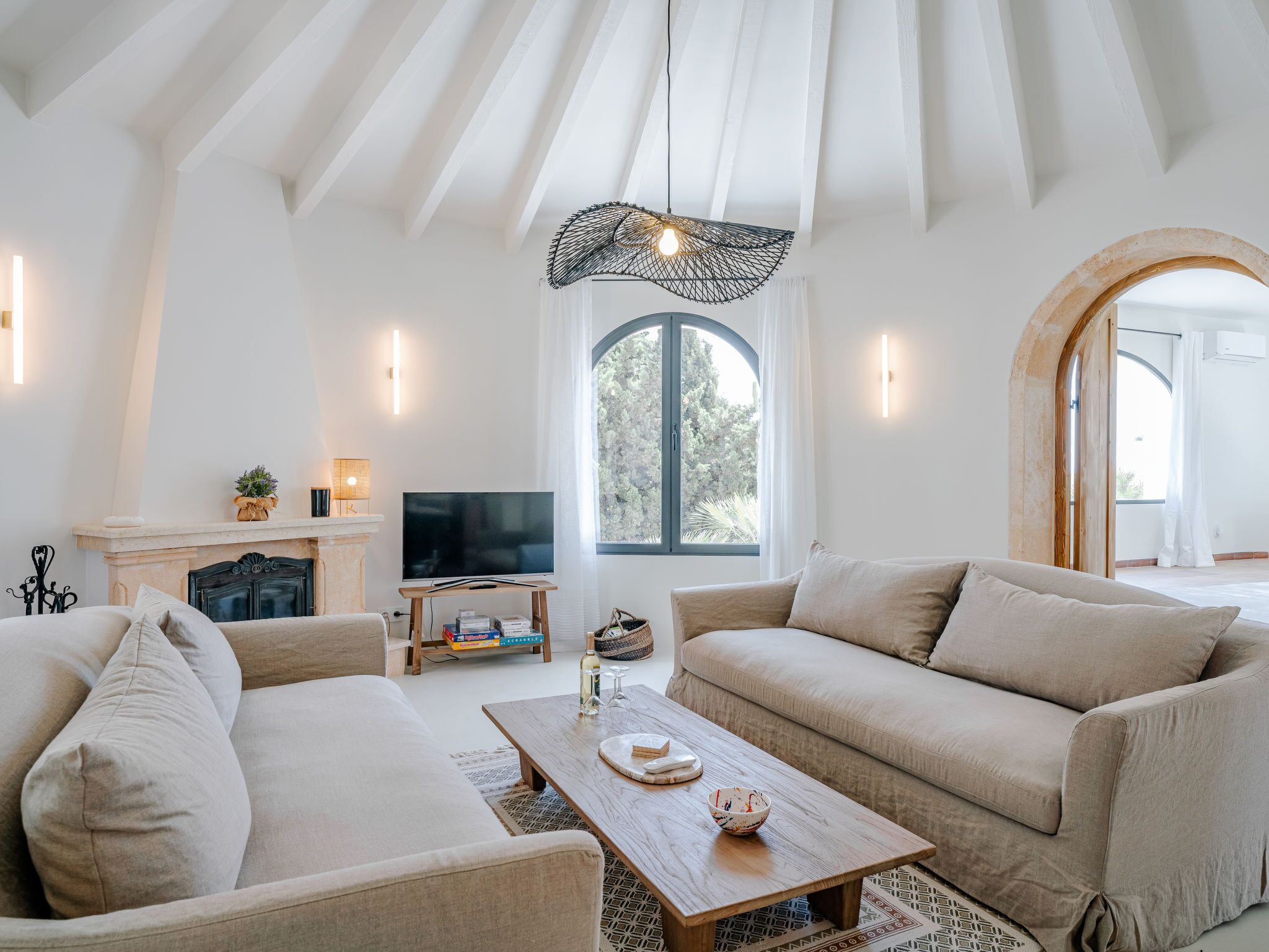 A spacious living room with a fireplace, a television, and a large window offering a view of trees.