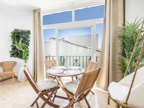 Ein Balkon mit rundem Tisch, Korbstühlen und einer hängenden Pflanze.