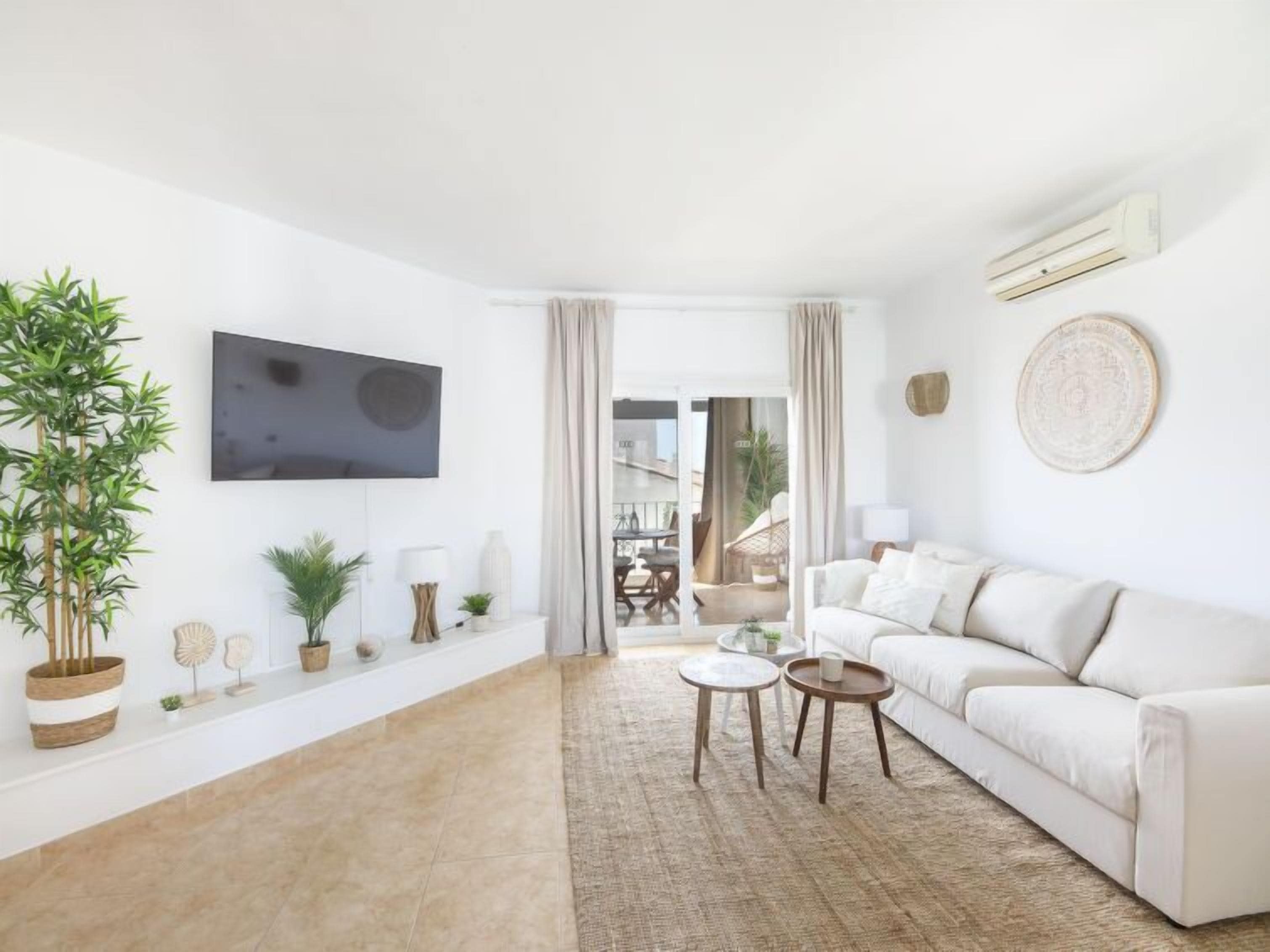 Ein modernes Wohnzimmer mit einem weißen Sofa, einem Flachbildfernseher und einer großen Topfpflanze.