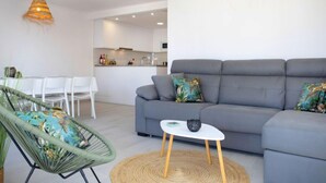 Ein modernes Wohnzimmer mit grauem Sofa, einem grünen Sessel, einem kleinen weißen Tisch und einer gewebten Leuchte.