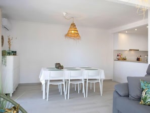 Et moderne spiseområde med et hvidt bord og stole, en hængende lampe og et køkken i baggrunden.