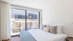 A bedroom with a large bed, a view through a sliding glass door to an outdoor area, and a small table beside the bed. - Premium Pestana Apartments (Porto)