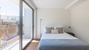 A bedroom with a large bed, a nightstand, a lamp, and a view of a balcony with a stone wall and railing. - Premium Pestana Apartments (Porto)