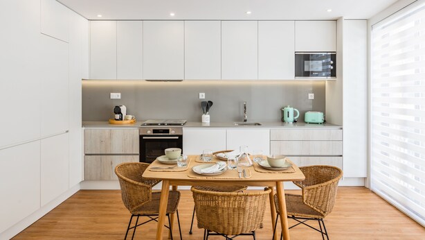 A modern kitchen with white cabinetry, a dining table set with plates and glasses, and a window with blinds. - Premium Pestana Apartments (Porto)