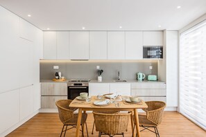 A modern kitchen with white cabinetry, a dining table set with plates and glasses, and a window with blinds. - Premium Pestana Apartments (Porto)