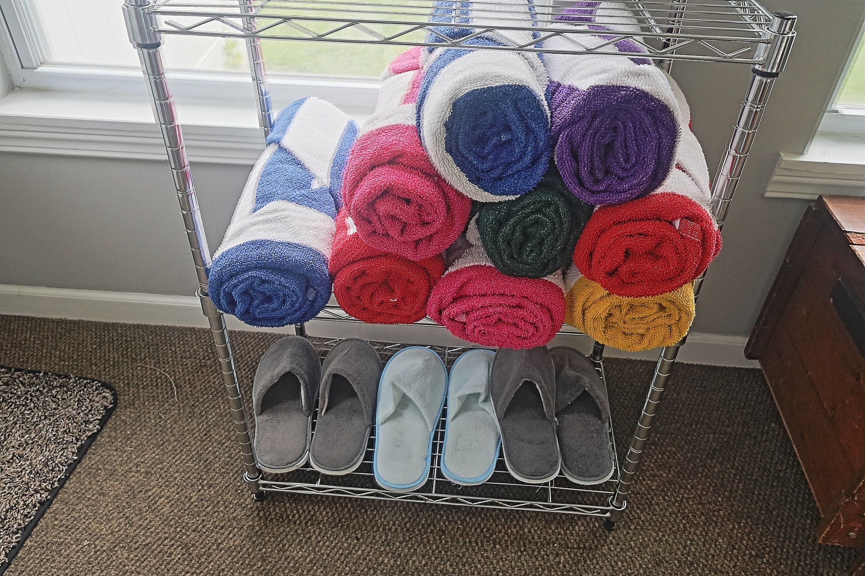 A metal rack with colorful towels and gray slippers.