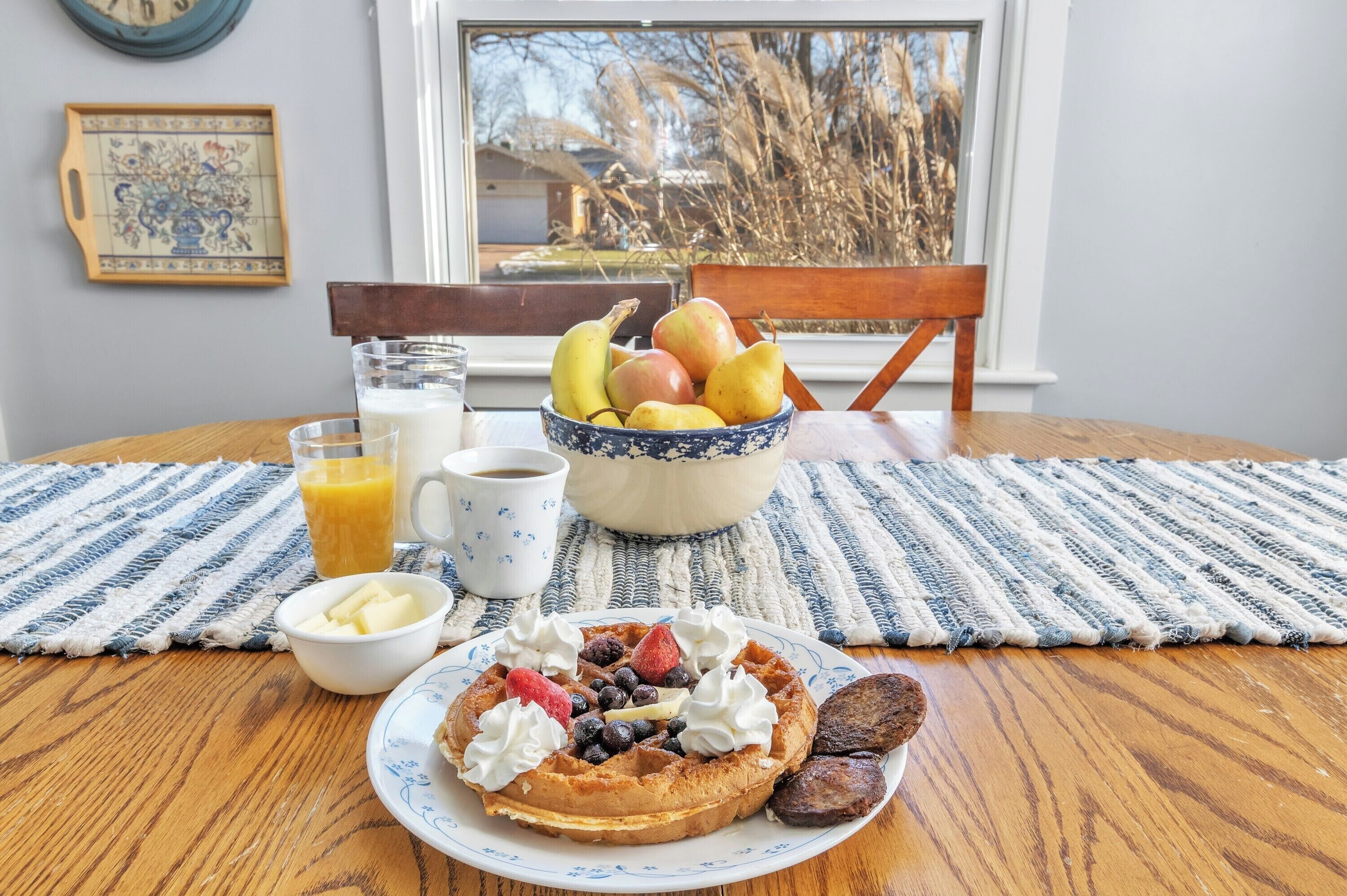 A breakfast setting with a waffle, fruit bowl, and beverages on a wooden table.