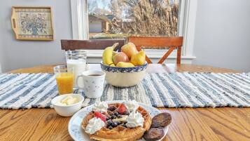 A breakfast setting with a waffle, fruit bowl, and beverages on a wooden table.