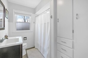 Un baño con lavamanos, inodoro y cortina de ducha blanca.
