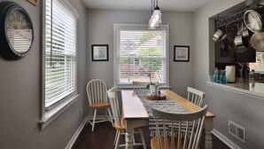 A dining area with a table, chairs, a hanging light fixture, and a window with blinds. - King room in Bed and Breakfast - And A Hot Tub! (FRANKENMUTH)