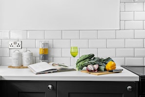 A kitchen counter with a coffee maker, tea kettle, a book, a glass of green liquid, vegetables, and a knife. - Coombe Bank (Teignmouth)