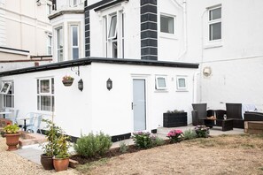 A white building with a black and white facade, a door, windows, outdoor seating, and potted plants.