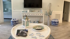 Una sala de estar con un televisor de pantalla plana montado en la pared, una mesa de centro con revistas y posavasos, y un farol decorativo.