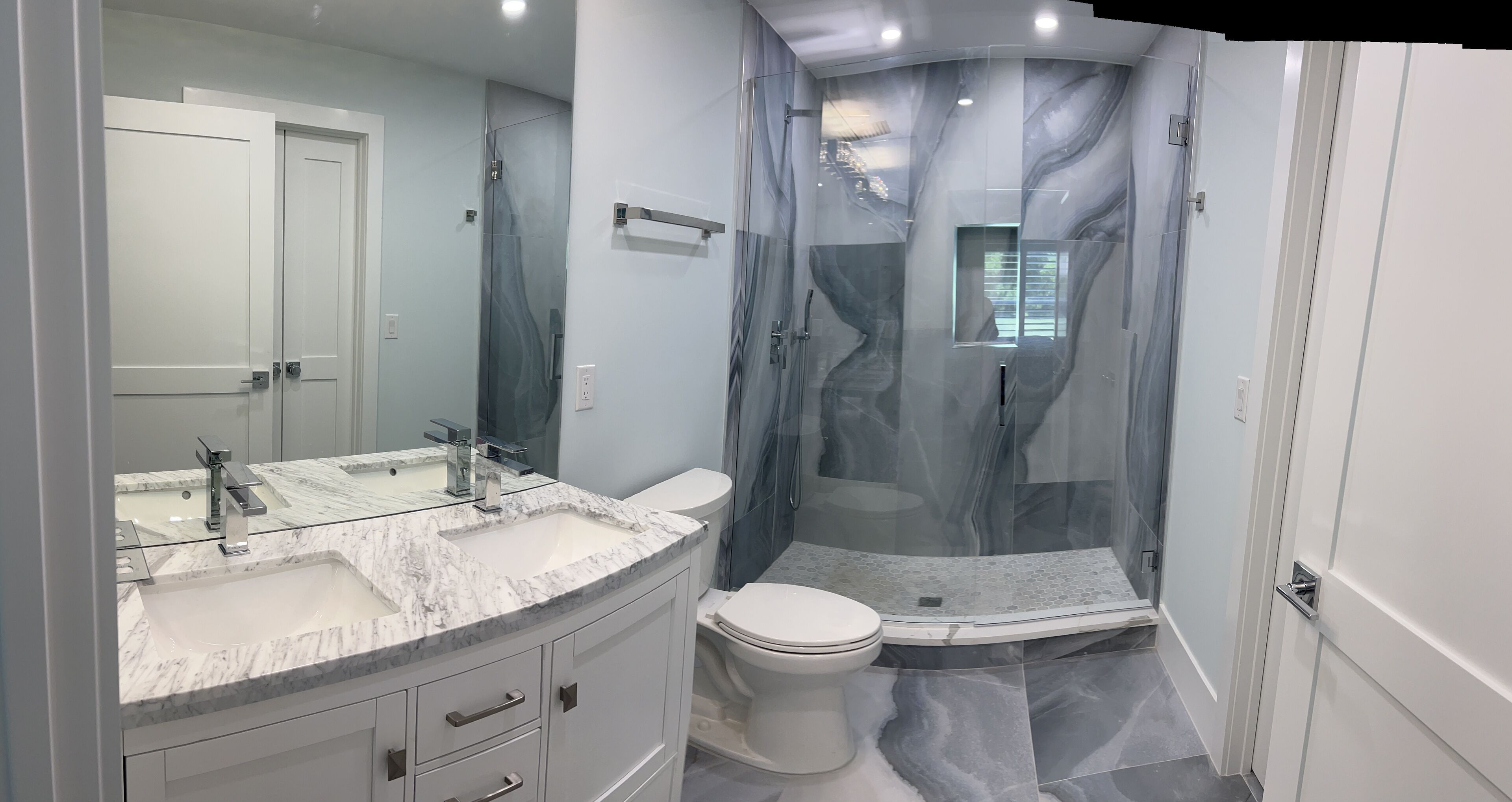 A modern bathroom with a glass-enclosed shower, a marble sink, and a toilet.