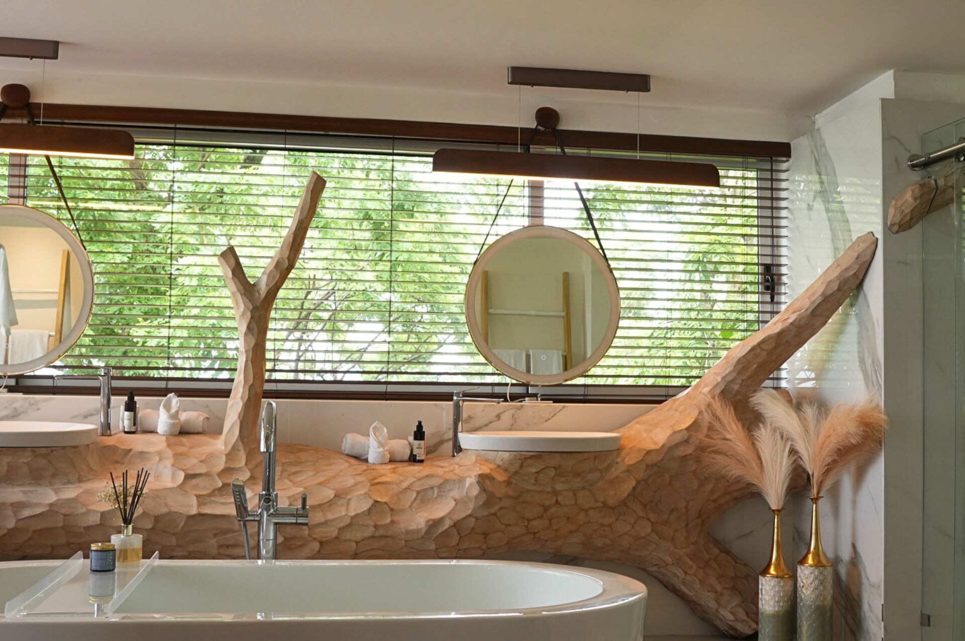A modern bathroom with a freestanding bathtub, two round mirrors, and a stone wall.