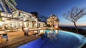 Ein modernes Haus mit Schwimmbad, Gartenmöbeln und Blick auf den Ozean im Abendlicht.