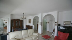 A spacious living room with a beige sofa, a red chair, a wooden cabinet, and a chandelier. - PescarHeart Apartment in the heart of Pescara (Pescara)