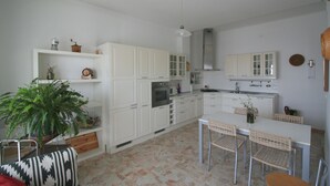 A compact kitchen with white cabinets, a built-in oven, and a dining area with a table and chairs. - PescarHeart Apartment in the heart of Pescara (Pescara)