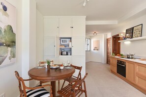 Una cocina moderna con muebles blancos, una mesa de comedor con sillas y un microondas.