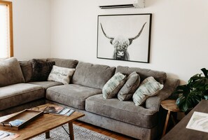 Een woonkamer met een grijze hoekbank, een houten salontafel en een lijst met een afbeelding van een stierenkop aan de muur.