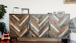 A wooden cabinet with a chevron pattern, a framed picture, and a 'BE HAPPY' sign on top.