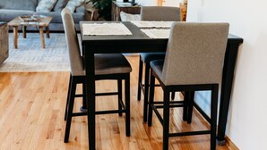 A dining area with a black table and four chairs, a wooden floor, and a grey sofa in the background.
