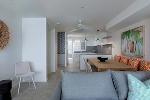 A modern living room with a sofa, a dining table, and a kitchen in the background.