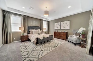 Cozy retreat with a large bed, nightstand, and dresser, plus a window and a small table with a potted plant.
