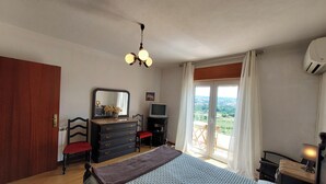 Quarto com cama, penteadeira, espelho, TV e varanda com vista.