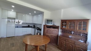 A kitchen with white cabinets, a wooden table, a stove, and a television on a wooden cabinet.