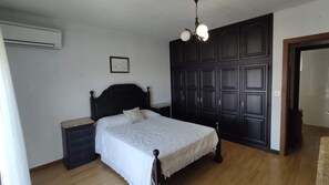 A bedroom with a bed, nightstand, wardrobe, and an air conditioning unit.