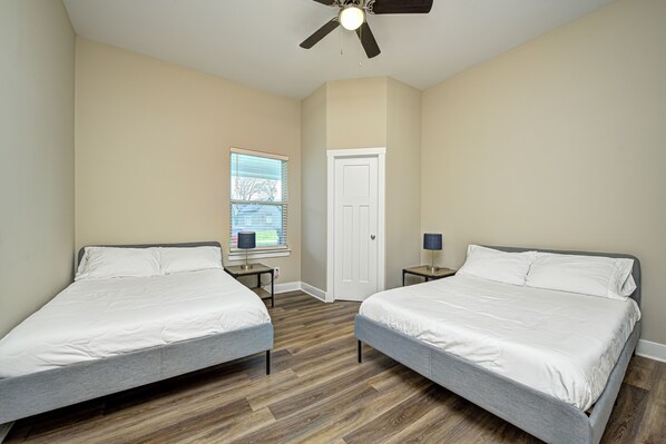 A bedroom with two beds, a ceiling fan, a window, and a door. - Centrally Located GEM Cozy & Close To Everything! (Indianapolis)