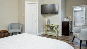 Un dormitorio con una cama, dos sillones, un televisor, un aparador y una puerta.