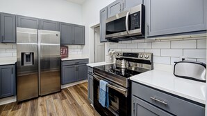 Una cocina moderna con electrodomésticos de acero inoxidable, gabinetes grises y encimera blanca.