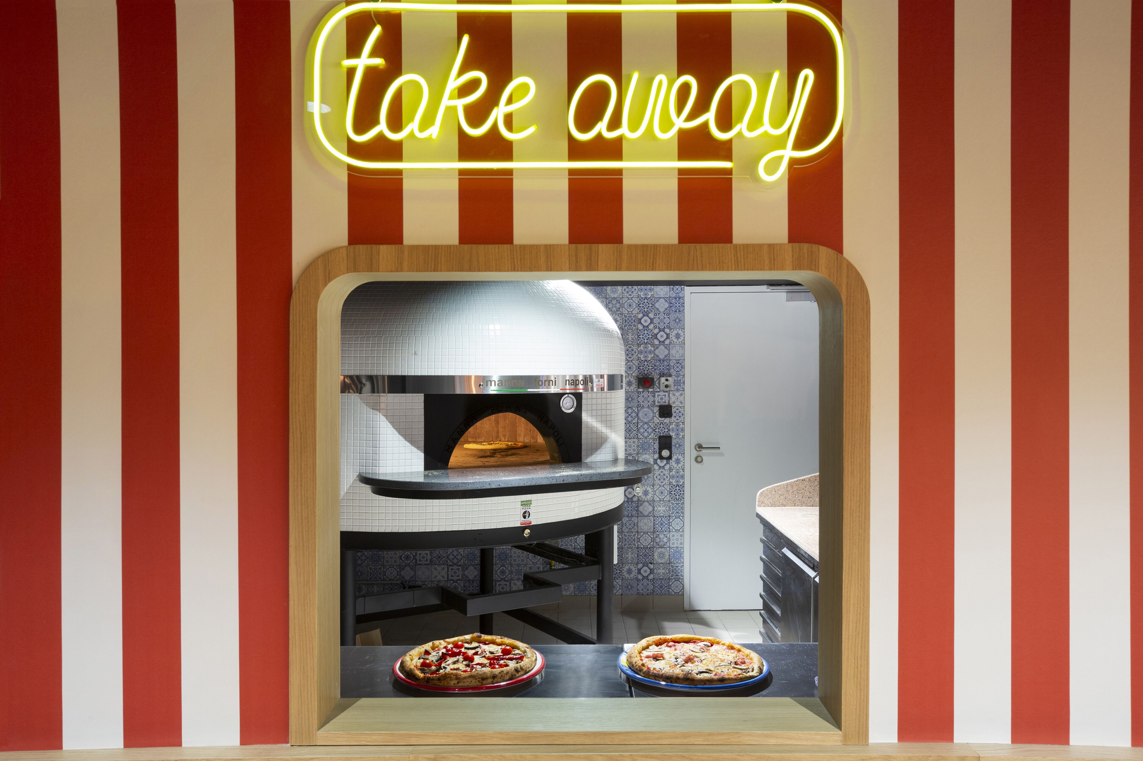 Een afhaalraam met een neonreclame, een oven en twee pizza's in de etalage.