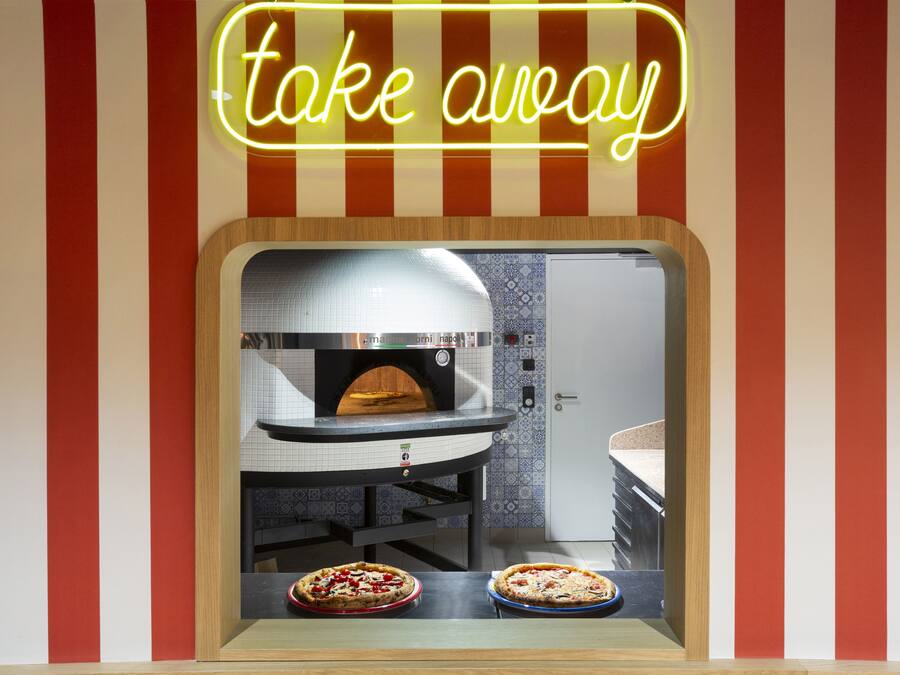 Een afhaalraam met een neonreclame, een oven en twee pizza's in de etalage.