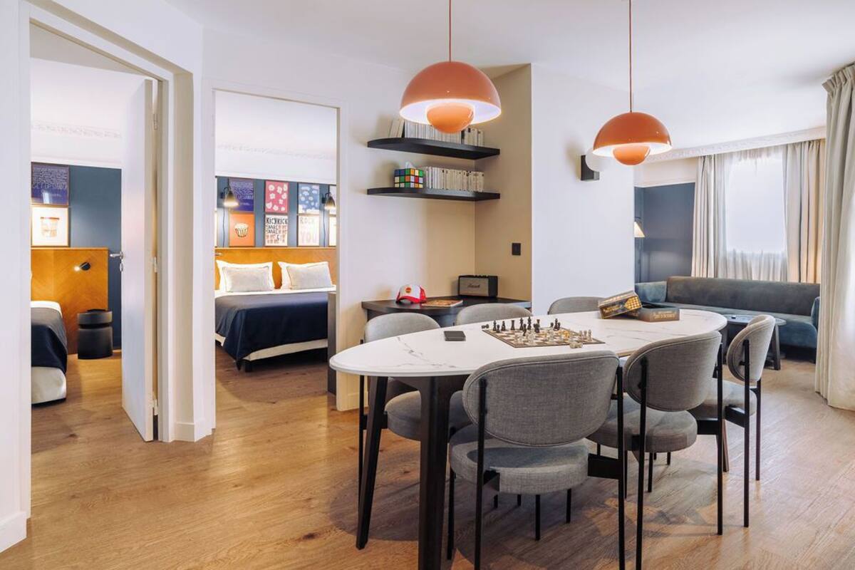Een moderne hotelkamer met een zithoek, een bed met hoofdeinde, een boekenkast en een groot raam met gordijnen.