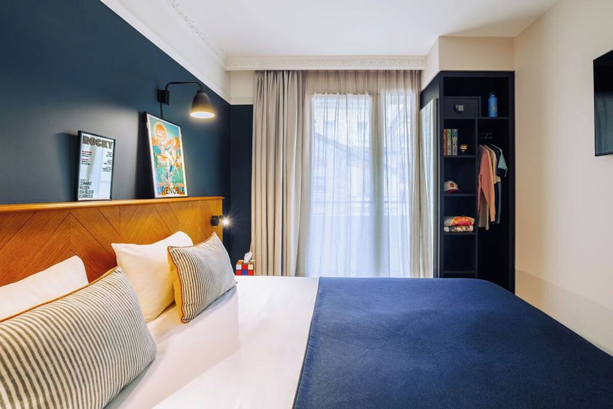 Een hotelkamer met een groot bed, een houten hoofdbord, een kledingkast en een raam met gordijnen.