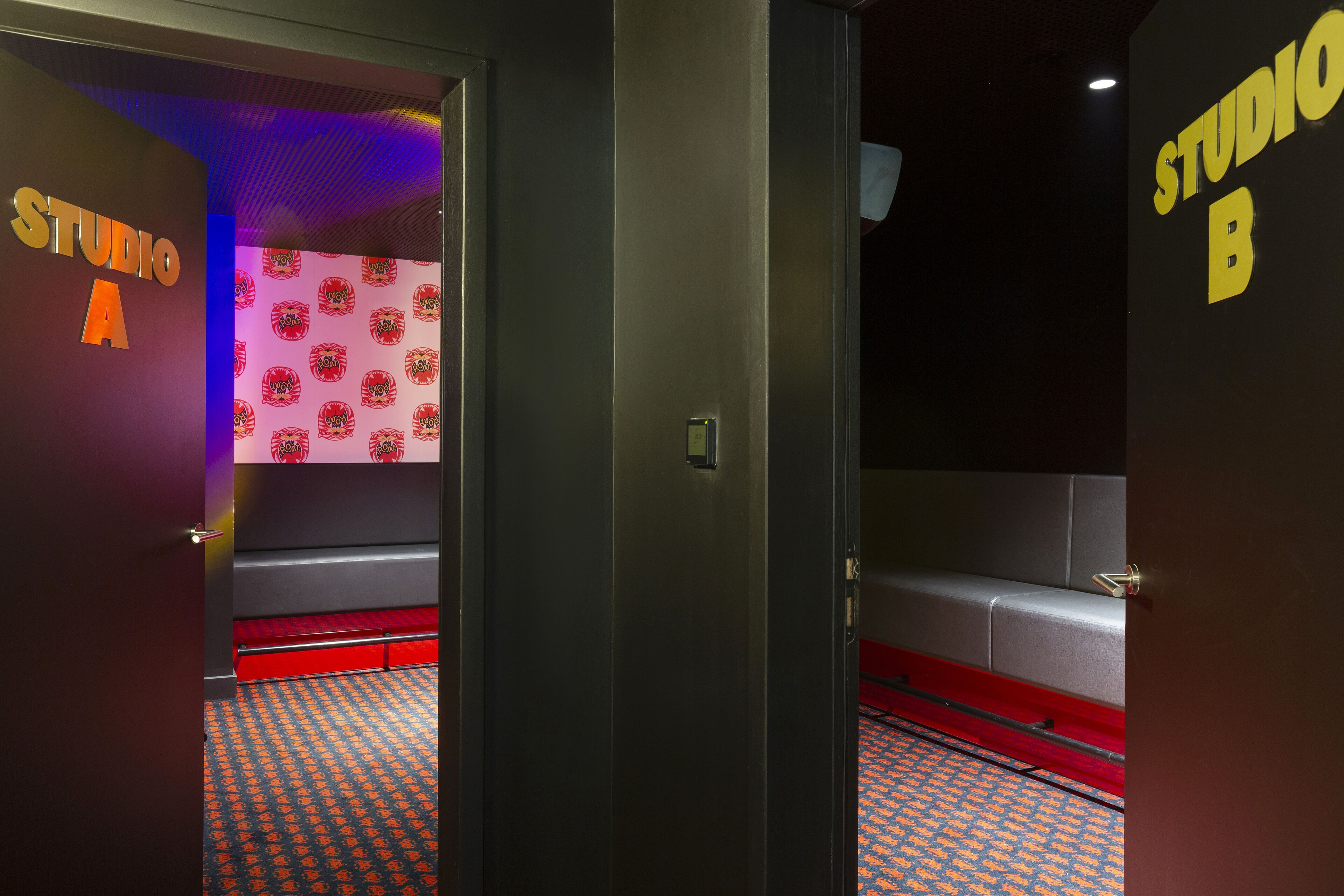 A hotel lobby with a red carpet, a seating area with red and grey upholstery, and walls with 'STUDIO A' and 'STUDIO B' signage.