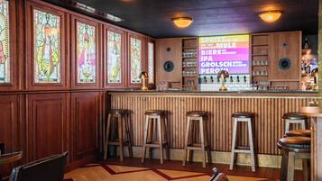 A bar area with wooden paneling, stained glass windows, and stools.