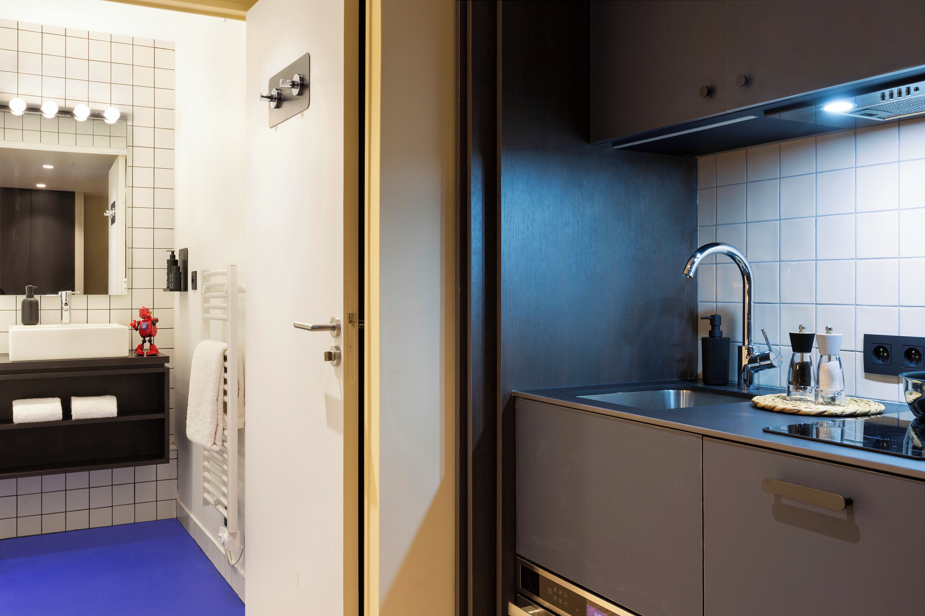 Een moderne badkamer met een grote spiegel, een wit wastafelmeubel en een blauwe vloer.