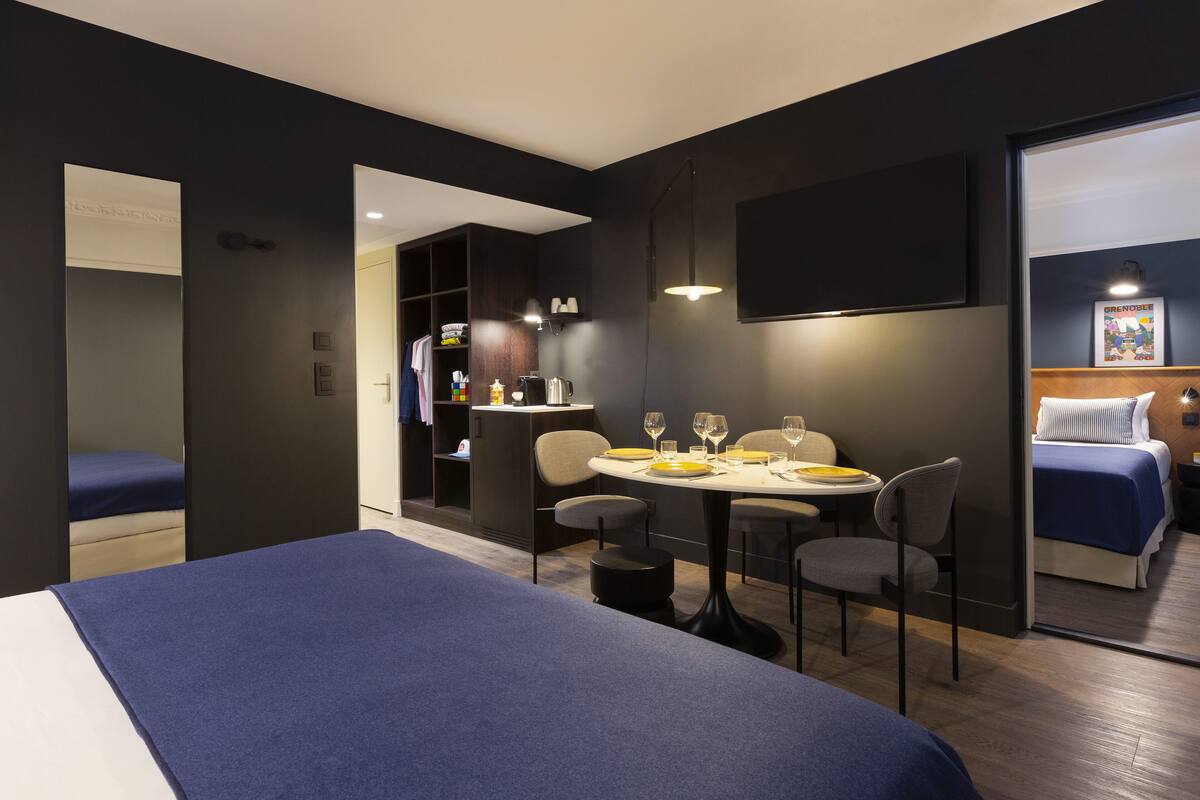 Een moderne hotelkamer met een groot bed, een zithoek met een tafel en stoelen, een kitchenette, en een afzonderlijke slaapruimte met een bed.