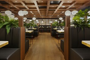 Un restaurante con vigas de madera en el techo, asientos tipo cabina acolchados de color negro y luces esféricas colgantes.