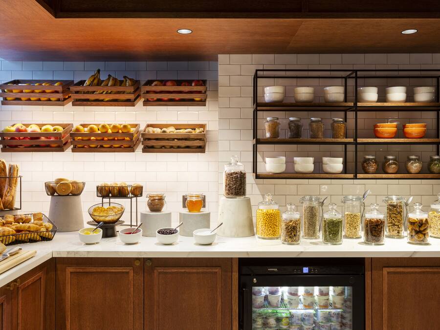 Una cocina con armarios de madera, un refrigerador y diversos alimentos en estantes y encimeras.