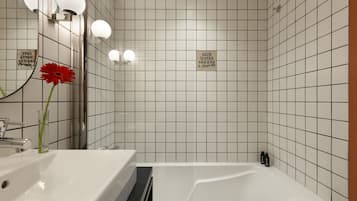 A modern bathroom with a white sink, a mirror, and a red flower. There is a sign that says "SAVE WATER SHOWER."