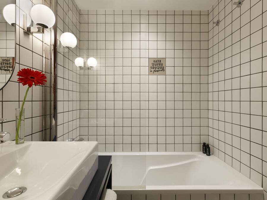 A modern bathroom with a white sink, a mirror, and a red flower. There is a sign that says "SAVE WATER SHOWER."