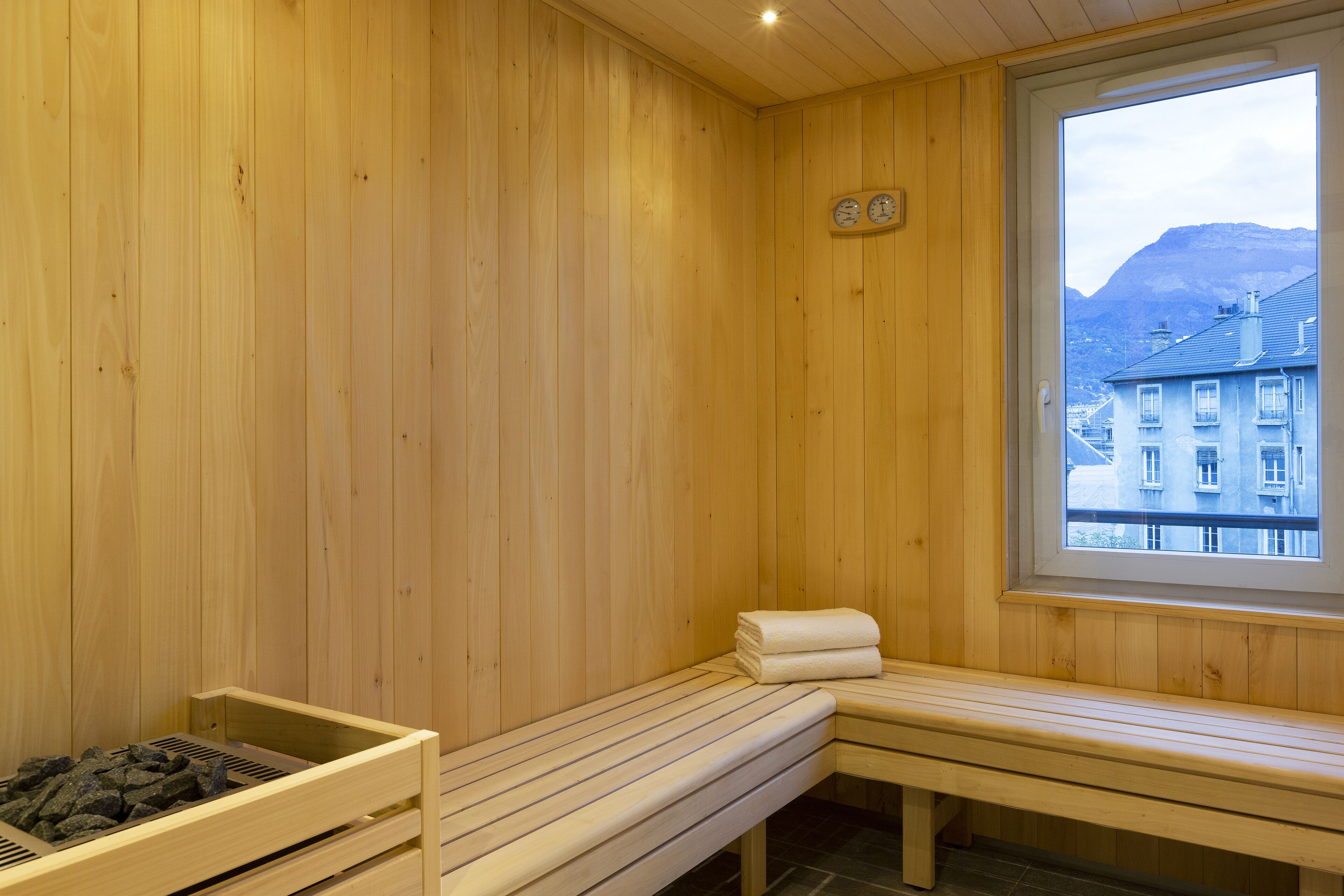 Een houten sauna met banken, een raam en uitzicht op gebouwen en bergen.