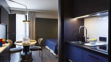 A modern hotel room with a dining area, a bed, and a kitchenette.
