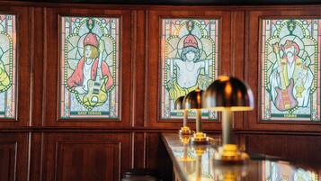 Een bar met houten lambrisering en glas-in-loodramen waarop muzikanten afgebeeld zijn.